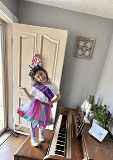 a little girl wearing a birthday sash stands on a piano