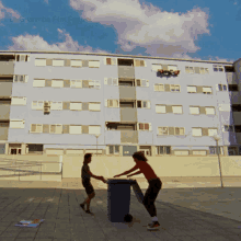 two people pushing a trash can in front of a building that says la guarimba film festival on the bottom