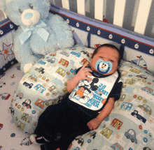 a baby wearing a bib that says mickey mouse is laying in a crib