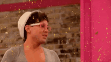 a man wearing glasses and a hat is standing in front of a pink door with confetti falling on him .