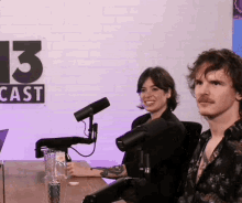 a man and a woman are sitting at a table in front of microphones with a sign that says 13 cast