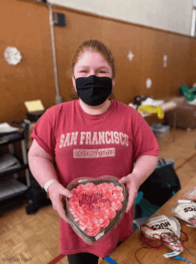 a girl in a san francisco shirt holds a heart shaped cake