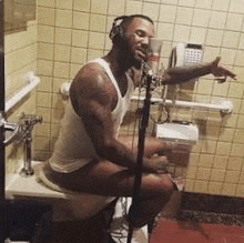 a man is sitting on a toilet in a bathroom singing into a microphone .