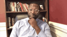 a man wearing glasses is sitting in front of a bookshelf with a book titled " a few dollars "