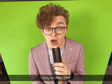 a man in a suit and glasses holds a hairbrush in front of a green screen that says " only in ohio oh "