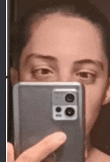 a woman is taking a selfie with her cell phone in front of her face .