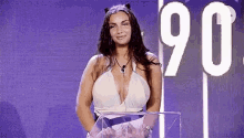 a woman in a plunging white dress is standing in front of a podium with the number 90 on it .