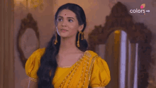 a woman in a yellow saree is standing in front of a mirror and looking up .