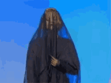 a woman in a black dress with a blue veil on her head is standing in front of a blue sky .