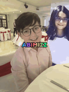 a boy wearing glasses sits at a table next to a picture of a girl with abimizz written on it