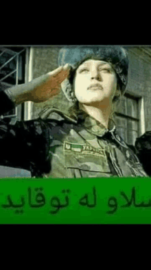 a woman in a military uniform salutes in front of a building with arabic writing .