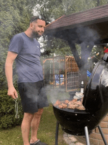 a man in a blue shirt is standing next to a grill with smoke coming out of it