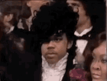 prince is wearing a tuxedo and a black hat and standing in a crowd of people .