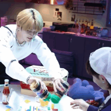 a man in a white shirt is pouring a bottle of ketchup on a table with a pizza box in the background