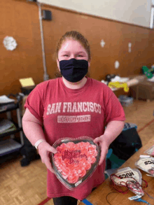 a girl wearing a red shirt that says san francisco is holding a heart shaped cake