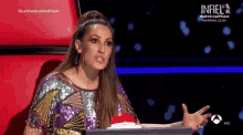 a woman in a sequined dress is sitting at a desk with a red button in front of her .