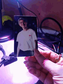 a person is holding a picture of a man in a white shirt with a red embroidered logo on it