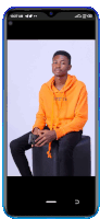 a young man in an orange hoodie is sitting on a black chair