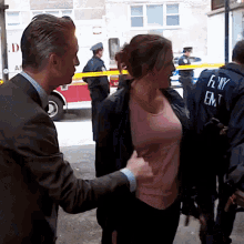 a man in a suit is touching a woman 's chest while a man in a fdny vest stands behind her