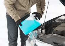 a man is pouring windshield washer fluid into the engine of a car .