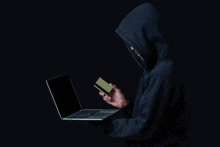 a man in a hoodie is holding a credit card and using a laptop computer