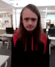 a young man with long hair is standing in a room with tables and chairs and looking at the camera .