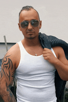 a man with a tattoo on his arm is wearing a white tank top and sunglasses