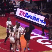 a group of women are playing basketball on a court with a sign in the background that says rw barrabas health .