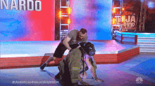 a man is wrestling a fireman on a stage with a nardo sign in the background