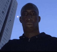 a man is standing in front of a tall building with the moon in the sky