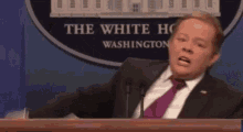 a man in a suit and tie is giving a speech at a podium in front of a white house .