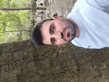 a man with a beard wearing a white nike shirt stands next to a tree