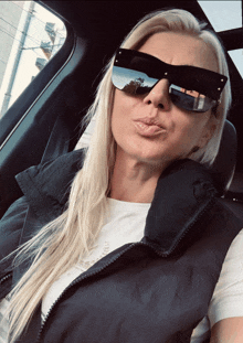 a woman wearing sunglasses and a black vest is sitting in the back seat of a car