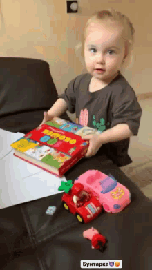 a little girl is sitting on a couch playing with toys and a book which says " kipovo " on it