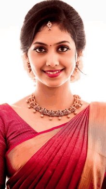 a woman wearing a red blouse and a gold necklace smiles for the camera