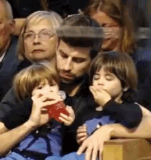 a man and two children are sitting in a stadium watching a game and one child is drinking from a red cup