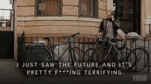 a man talking on a cell phone while standing in front of a brick building with bikes parked in front of it