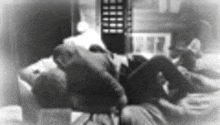 a black and white photo of a person laying on a couch with a remote control in the background .