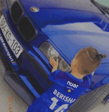 a little boy in a blue jersey is standing next to a blue car .