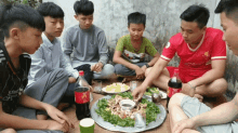 a group of young men are sitting around a plate of food with a coca cola bottle in front of them