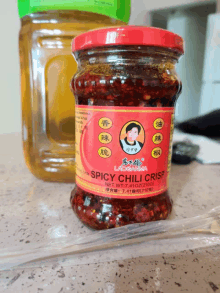 a jar of spicy chili crisp sits on a table next to a bottle of oil