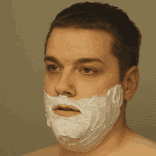 a man with a shaving cream on his face looks at the camera