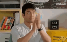 a man in a white shirt is clapping his hands while sitting in a chair in front of a bookshelf .