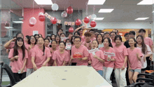 a group of people wearing pink shirts are posing for a picture with balloons and a banner that says happy birthday