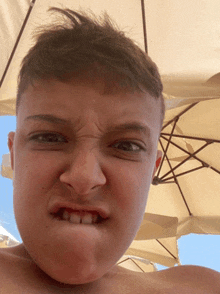 a young boy making a funny face in front of a tan umbrella