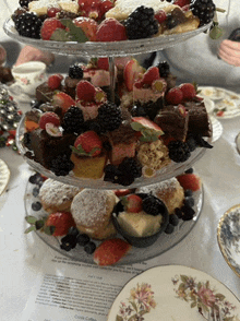 a three tiered display of desserts with strawberries and blackberries on top