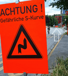 an orange sign says achtung gefahrliche s-kurve on it