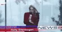 a woman is holding a microphone in front of a news screen with holly ellenbogen written on it .