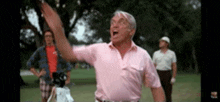 a man in a pink shirt is standing on a golf course with his arms outstretched