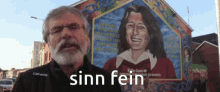 a man stands in front of a mural with the words sinn fein on the bottom